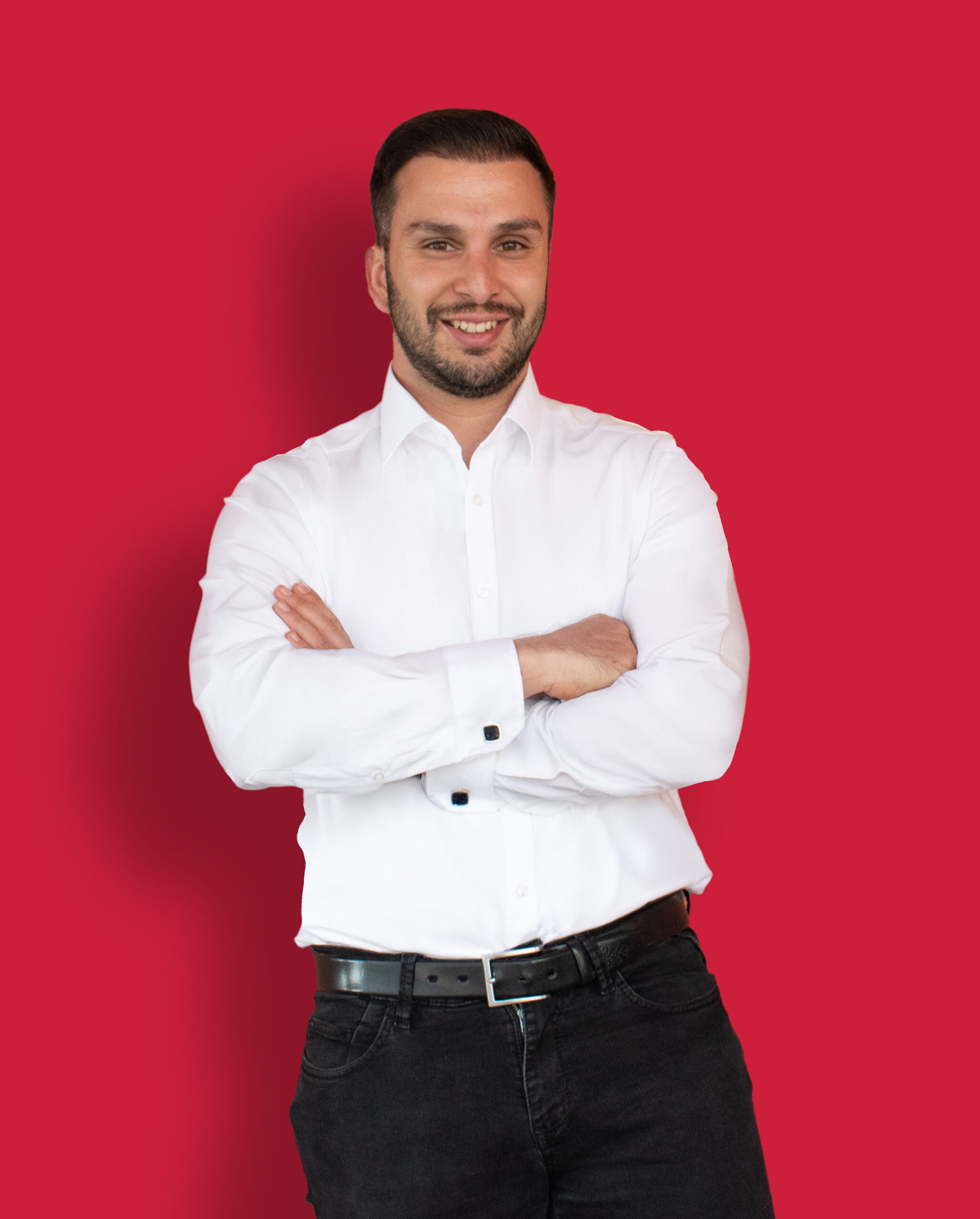 Porträtfoto des Business Coaches Ali Tumani in einem weißen Hemd vor einem roten Hintergrund.